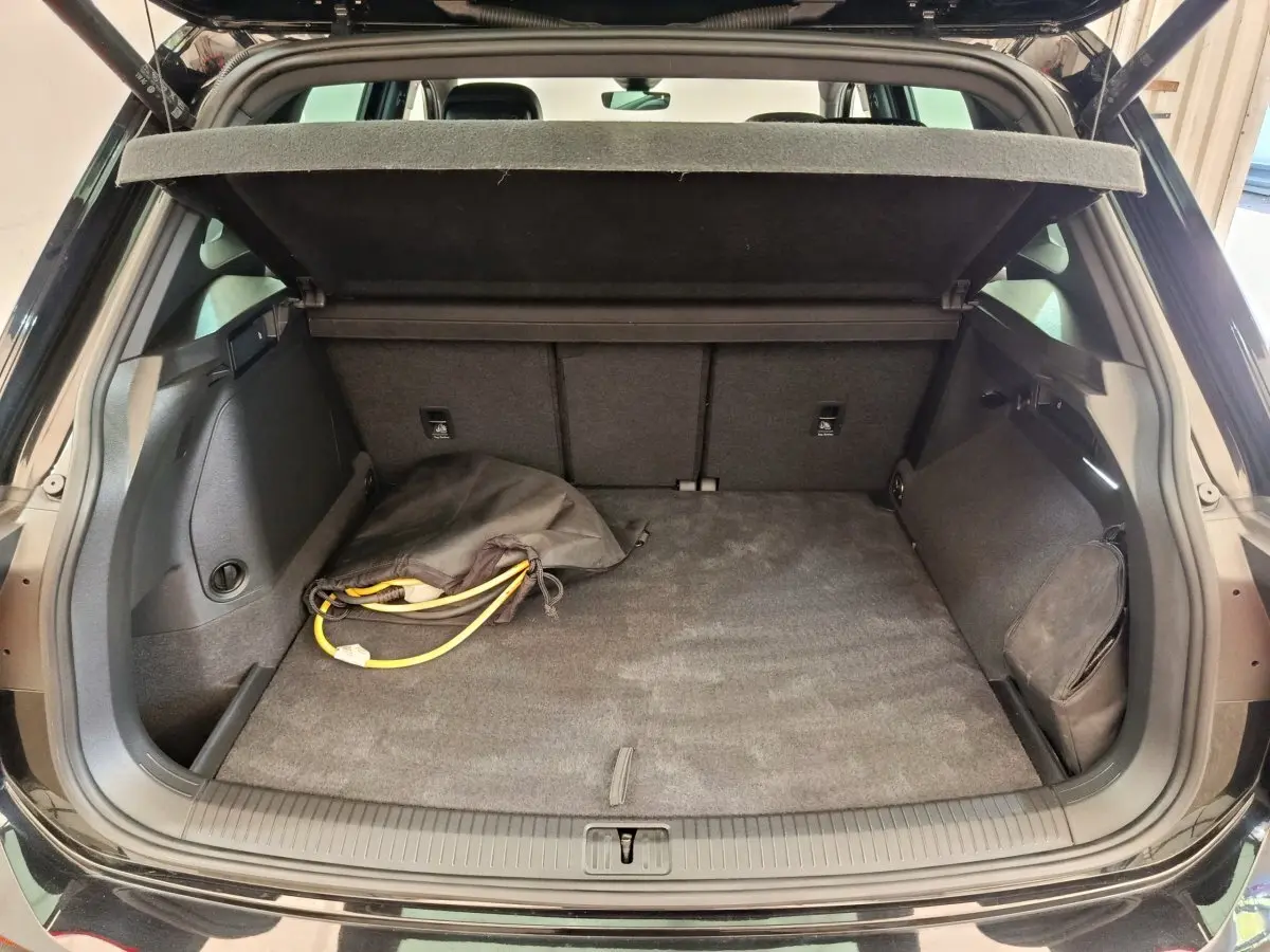 Coffre ouvert d’un Volkswagen Tiguan noir 2023, vue arrière, avec câble de recharge et cache-bagages déployé.