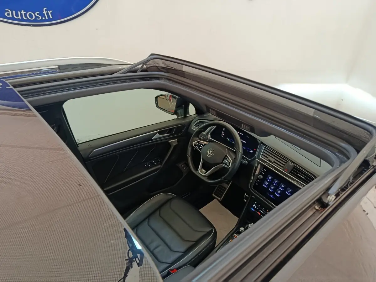 Vue intérieure par le toit ouvrant du Volkswagen Tiguan noir, mettant en valeur le volant cuir et l'écran tactile central.