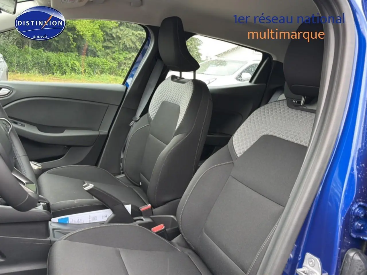 Vue intérieure côté conducteur de la Renault Clio V bleu iron, mettant en valeur les sièges avant bicolores et la console centrale.