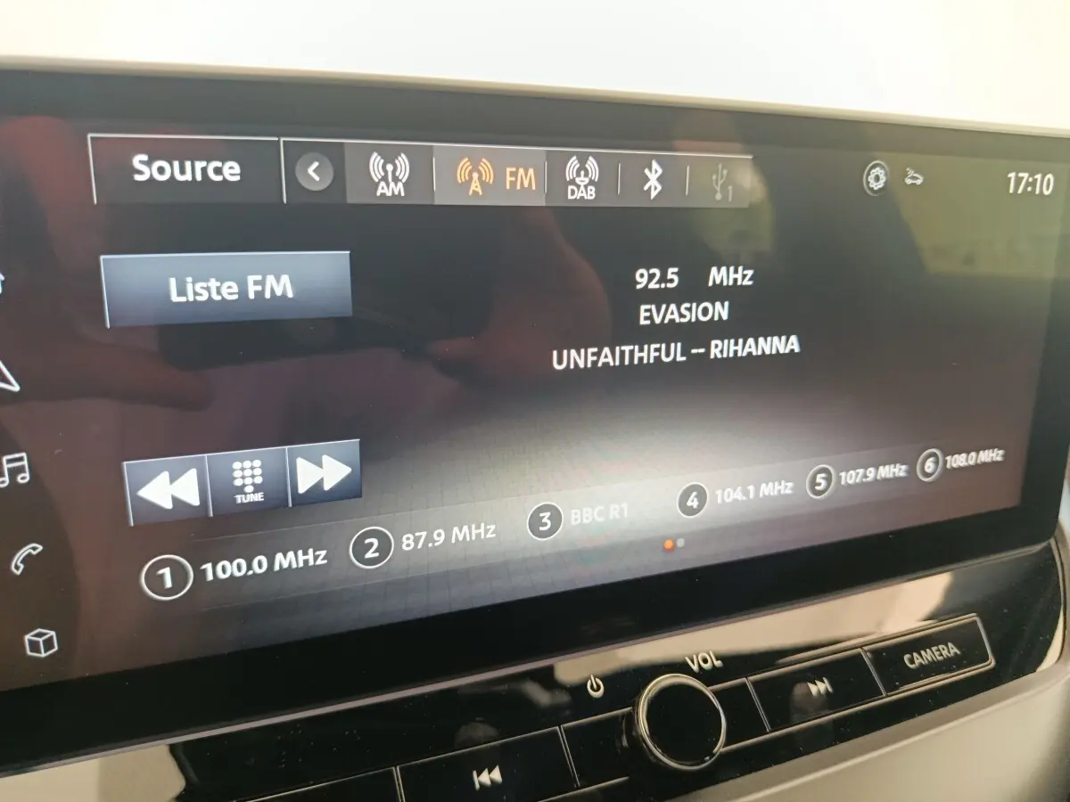Écran tactile central du Nissan Juke bleu 2025 affichant la radio FM avec station et titre de chanson visibles.
