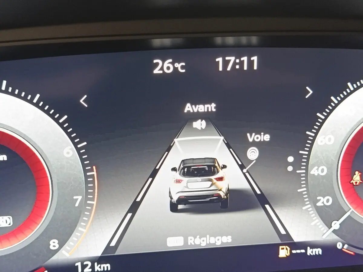 Affichage numérique du tableau de bord montrant une voiture blanche vue de dos avec alertes de voie et température à 26°C.