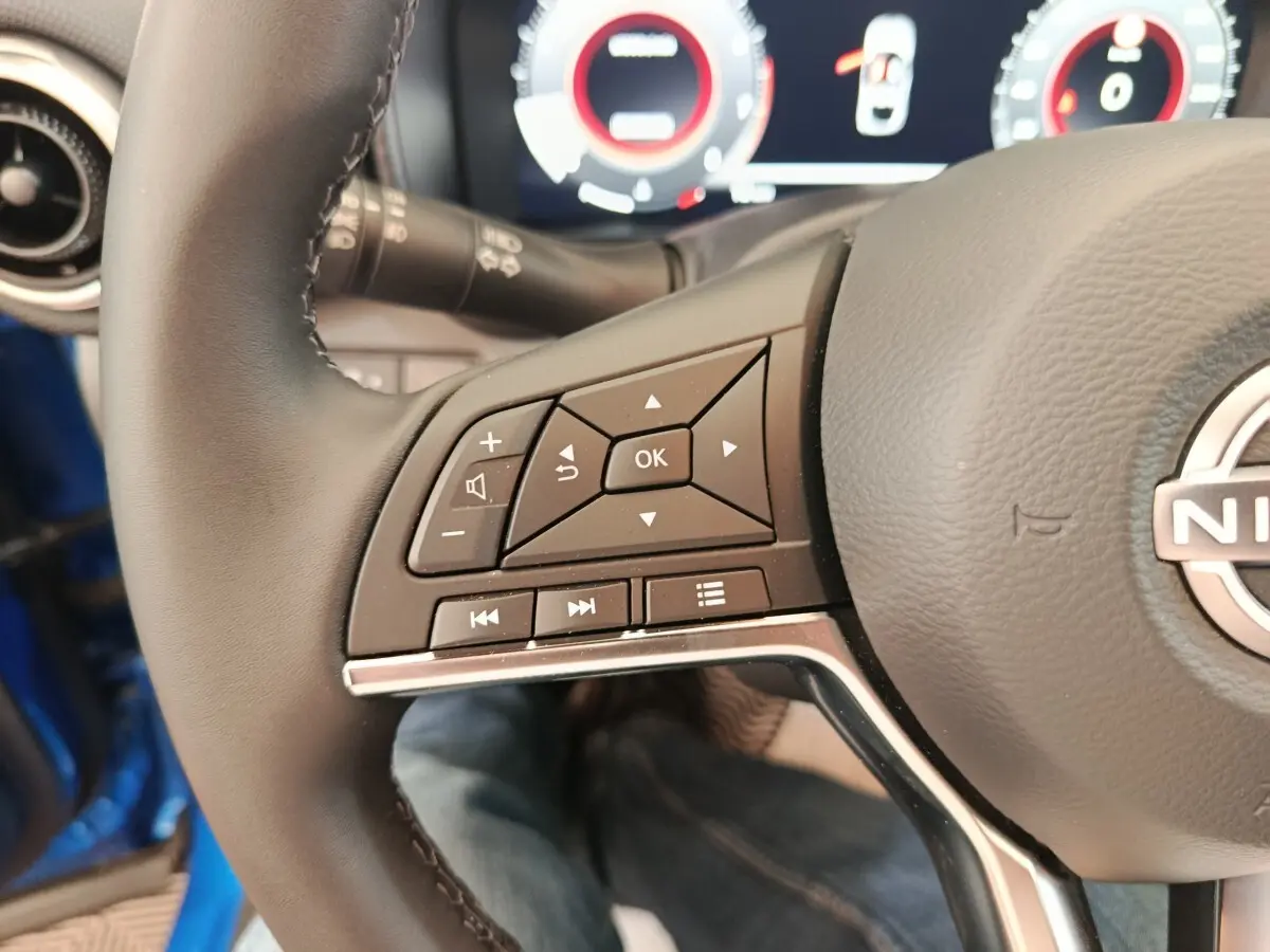 Gros plan sur les commandes gauche du volant cuir du Nissan Juke bleu, avec affichage numérique en arrière-plan.