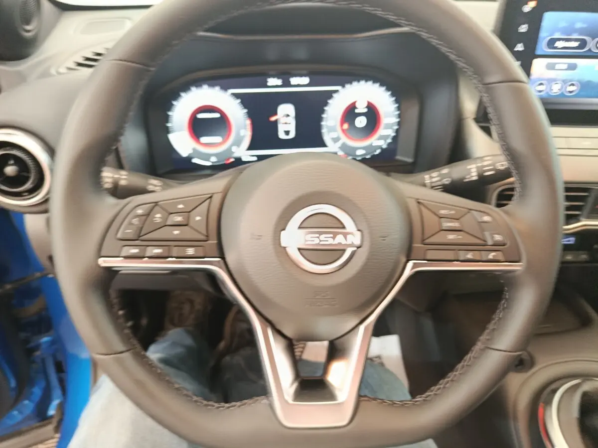 Vue rapprochée du volant cuir noir du Nissan Juke bleu 2025 avec tableau de bord numérique et écran tactile central.