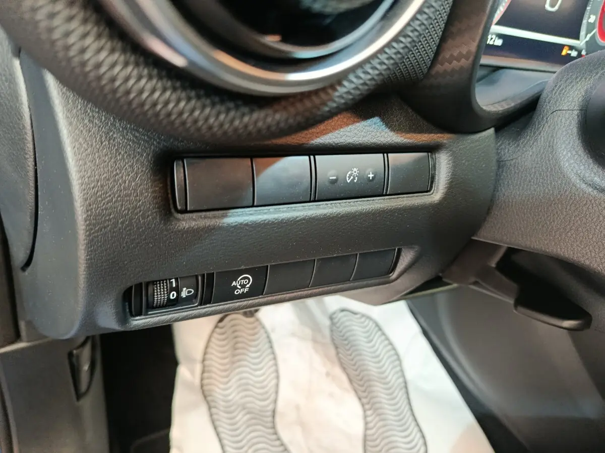 Détail des commandes d’éclairage et réglages au tableau de bord côté gauche du Nissan Juke bleu 2025.