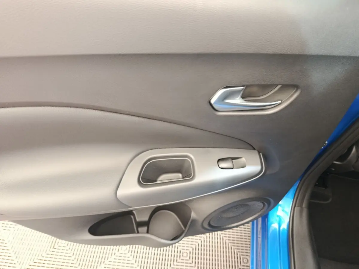 Intérieur côté droit de la porte avant d’un Nissan Juke bleu 2025 avec poignée argentée et haut-parleur intégré.