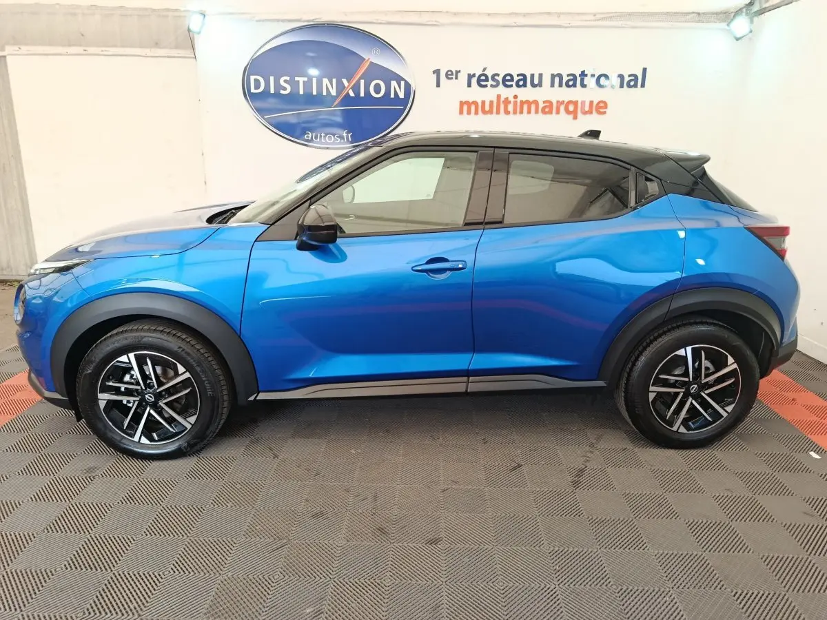 Vue de profil côté gauche d'un Nissan Juke bleu 2025 avec toit noir et jantes alliage bicolores.