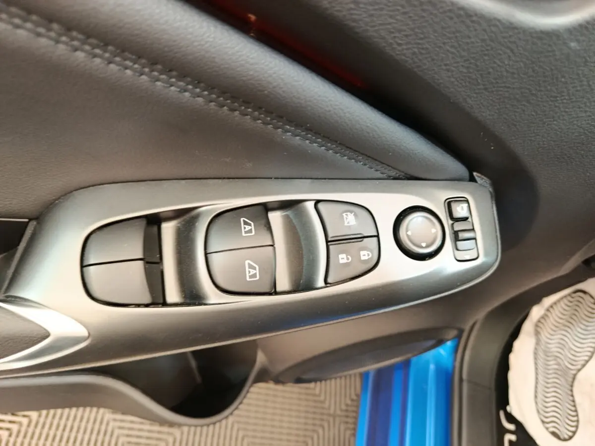 Gros plan sur les commandes des vitres et rétroviseurs côté conducteur du Nissan Juke bleu 2025, intérieur noir.