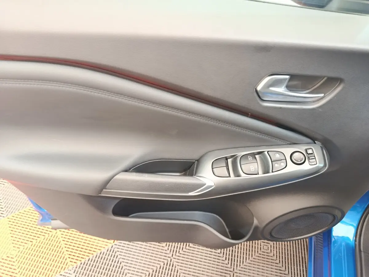Vue intérieure côté gauche de la porte avant d’un Nissan Juke bleu avec commandes de vitres et poignée argentée.