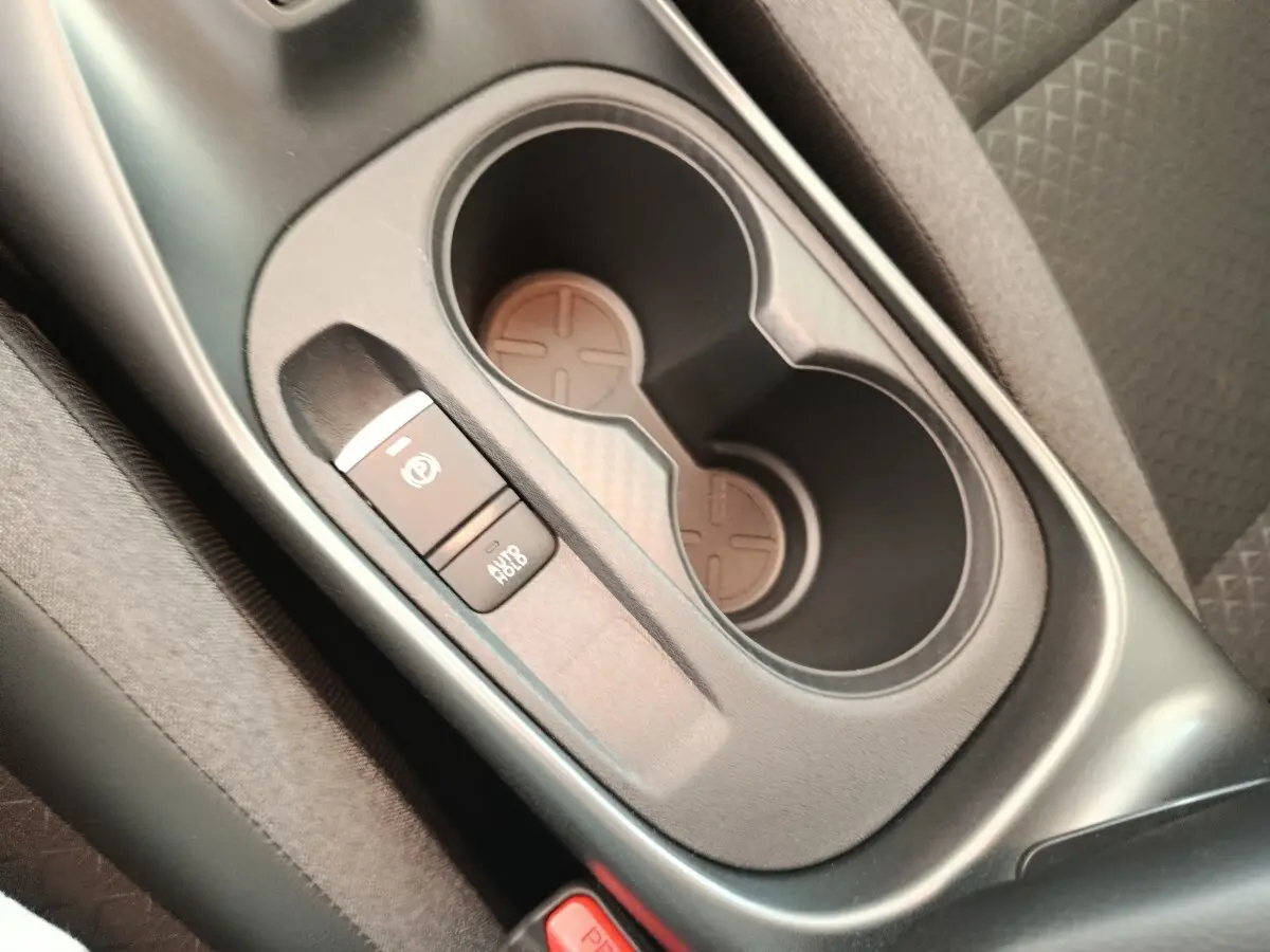 Gros plan sur la console centrale noire du Nissan Juke bleu 2025, avec porte-gobelets et frein à main électrique.
