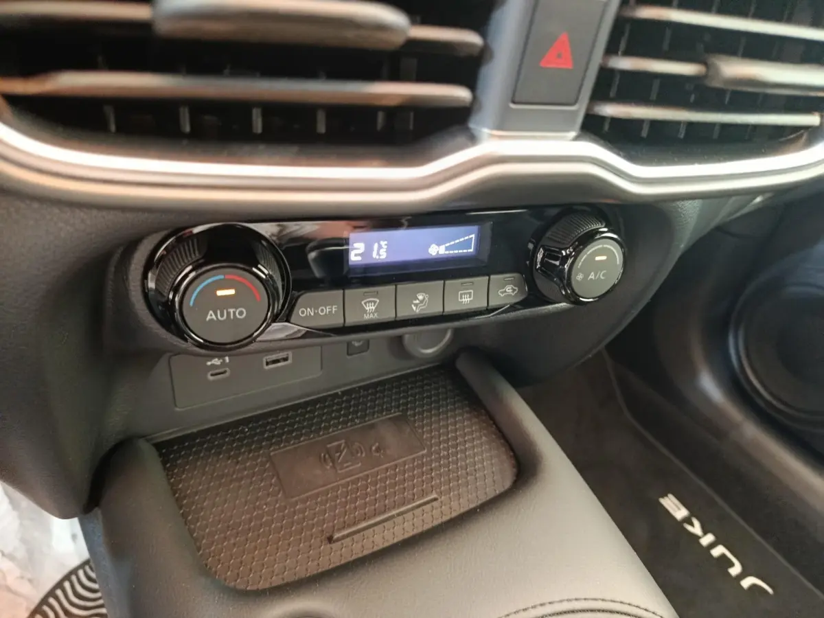 Détail de la console centrale du Nissan Juke bleu 2025, montrant les commandes de climatisation et un espace de recharge sans fil.