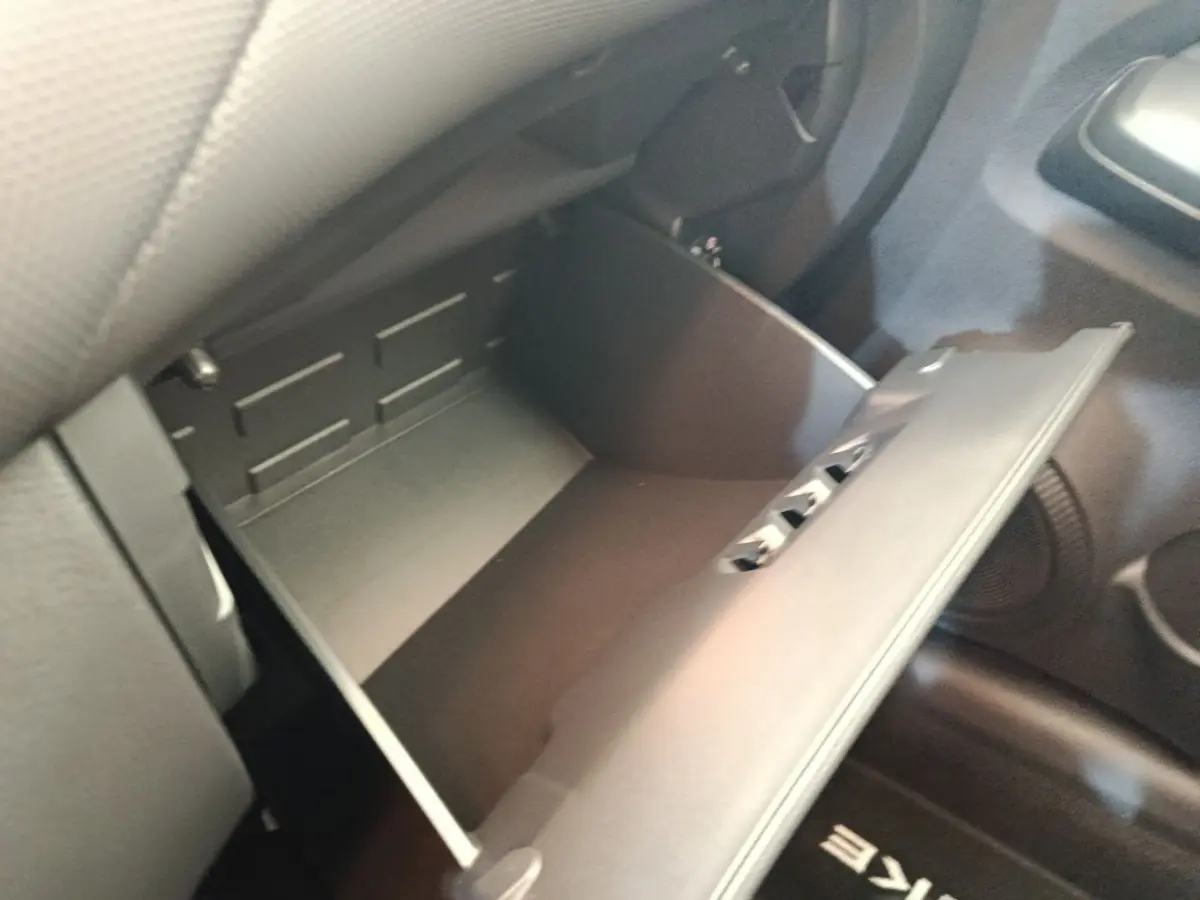 Vue rapprochée de la boîte à gants ouverte côté passager dans l’habitacle noir du Nissan Juke bleu 2025.