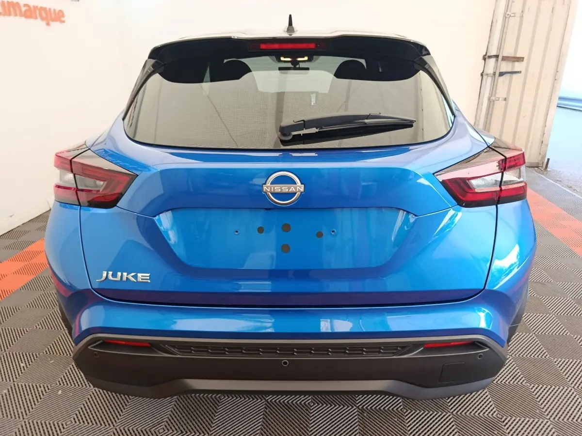 Vue arrière d'un Nissan Juke bleu 2025 avec feux LED et logo Nissan bien visibles sur un sol à damier.