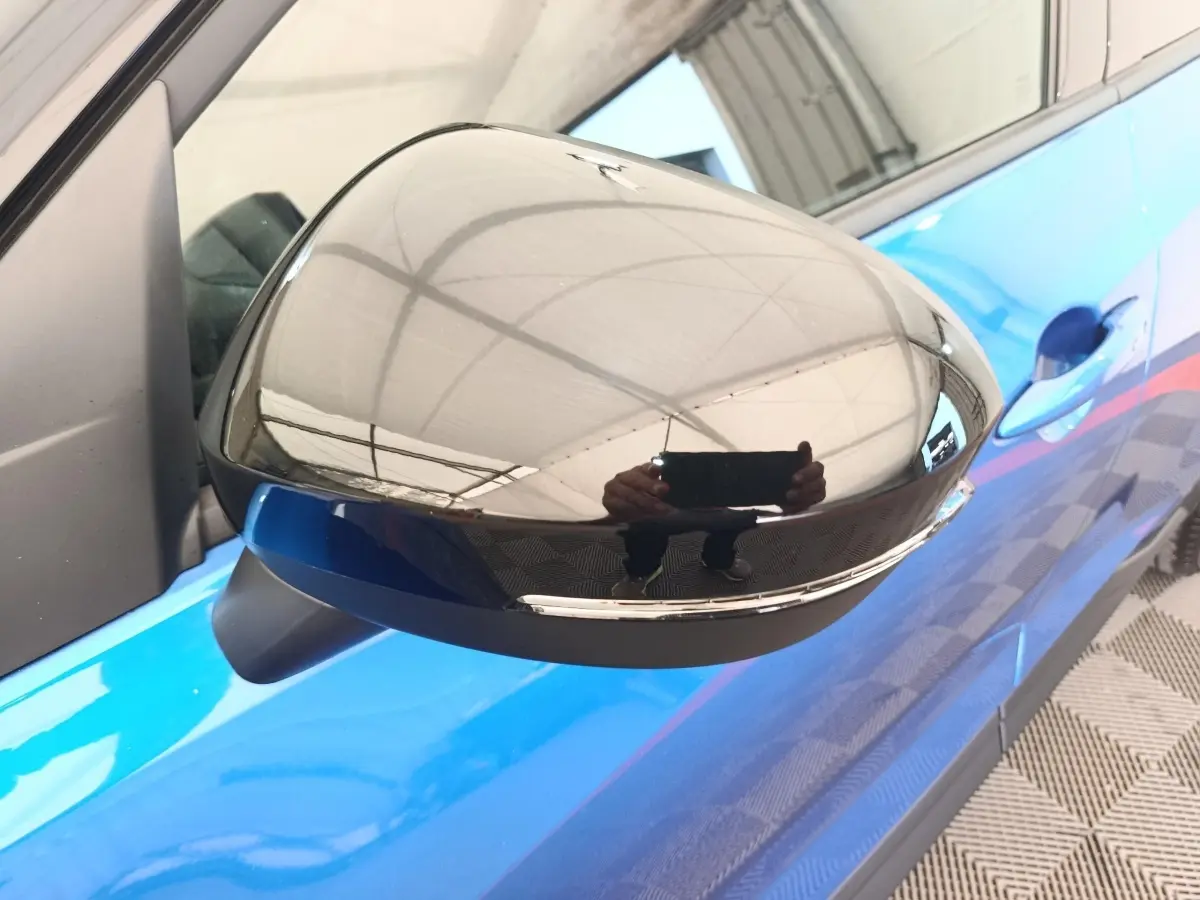 Gros plan sur le rétroviseur droit noir brillant du Nissan Juke bleu, avec poignée de porte visible en arrière-plan.