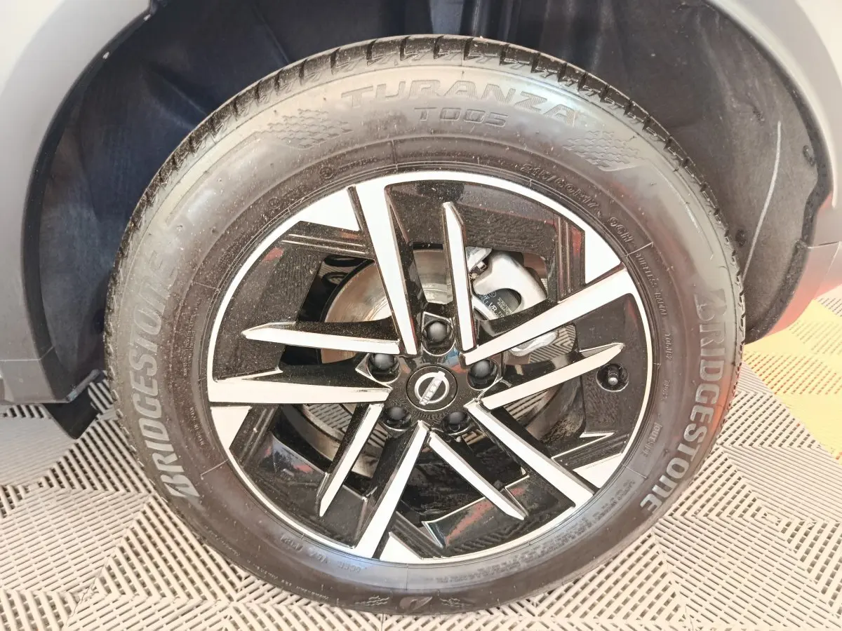 Gros plan sur la jante alliage noire et argentée du Nissan Juke bleu, mettant en valeur le logo Nissan central.