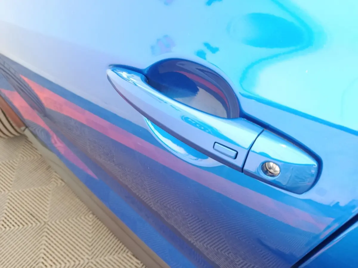 Gros plan sur la poignée de porte côté droit bleu vif du Nissan Juke DIG-T 114 BVM6 N-Connecta 2025.