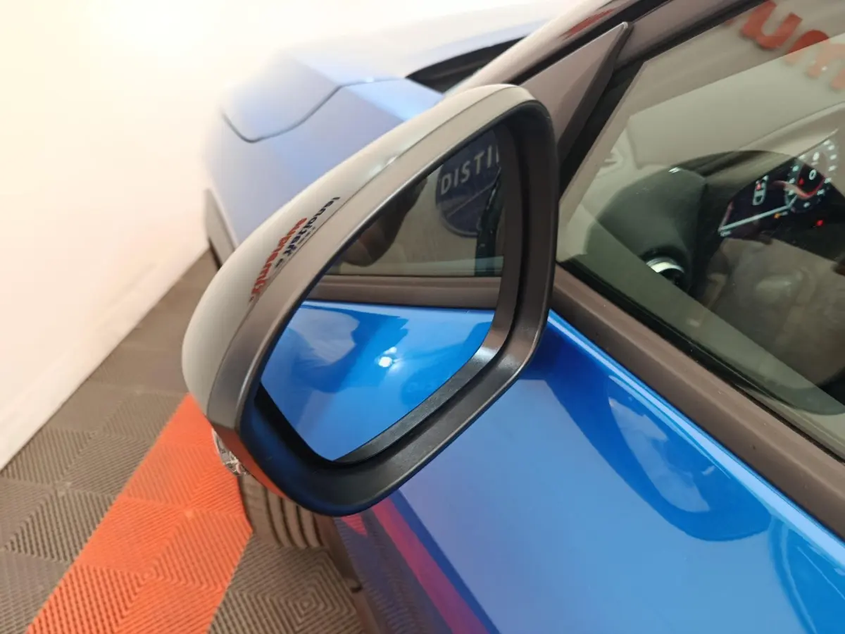 Rétroviseur côté gauche en gros plan sur Nissan Juke bleu, avec intérieur et tableau de bord partiellement visibles.