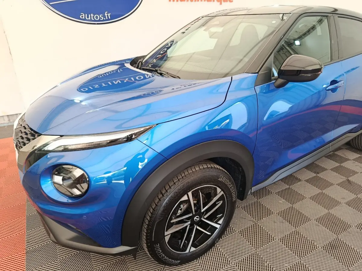 Vue 3/4 avant droit du Nissan Juke bleu 2025 avec phares ronds et jantes noires à motif argenté.