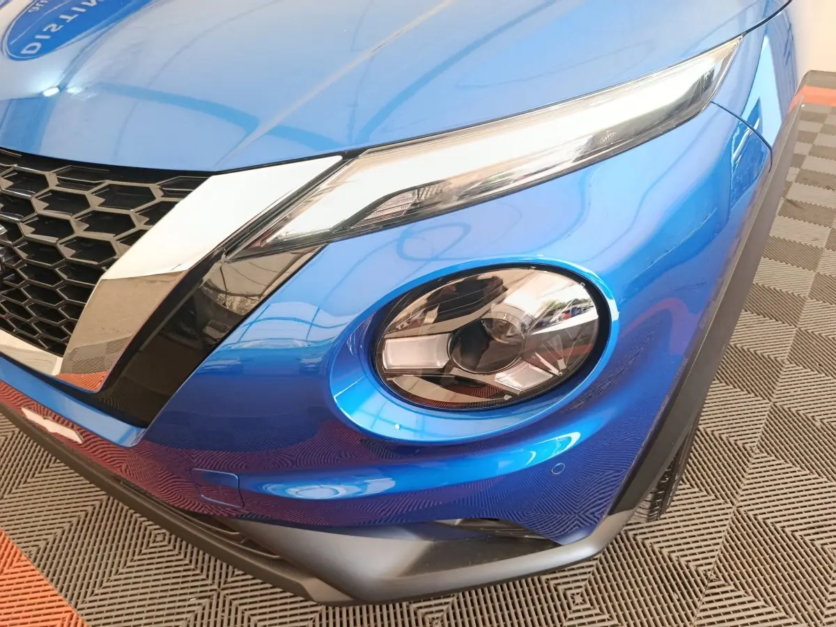 Gros plan sur le phare avant droit bleu vif du Nissan Juke 2025 avec calandre noire et détails chromés.