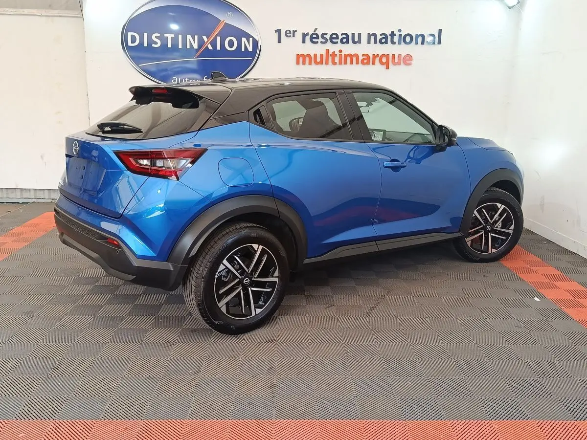Vue 3/4 arrière droite d'un Nissan Juke bleu 2025 avec toit noir et jantes alliage bicolores.
