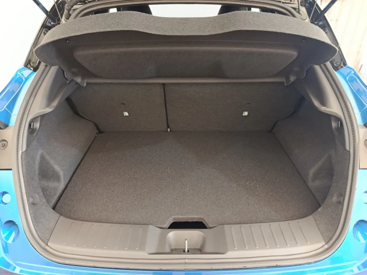Coffre ouvert vu de l'arrière du Nissan Juke bleu 2025, espace de chargement propre et vide, banquette arrière visible.