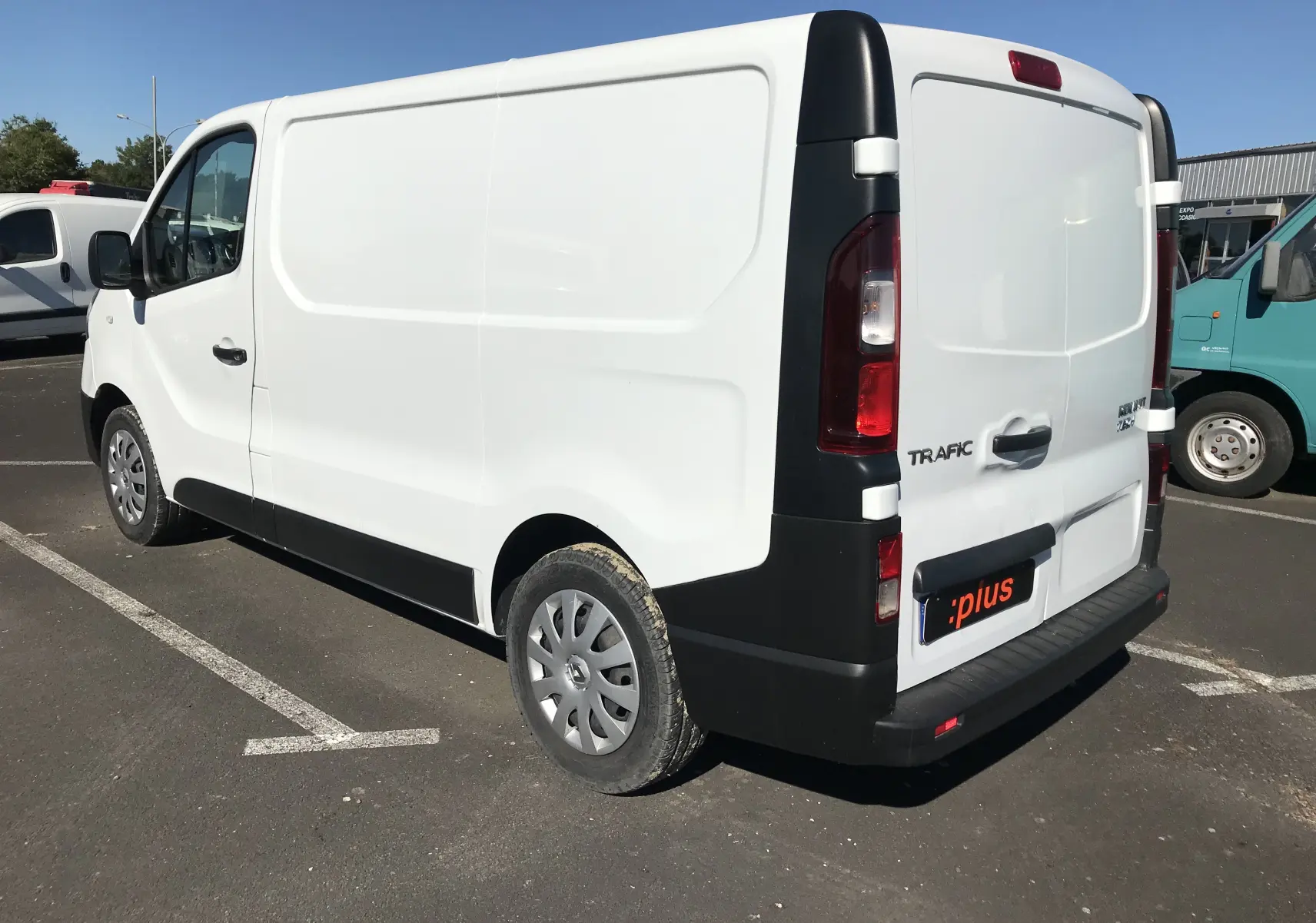Renault Trafic Fourgon blanc vu en 3/4 arrière droit, avec porte latérale coulissante et hayon fermé.