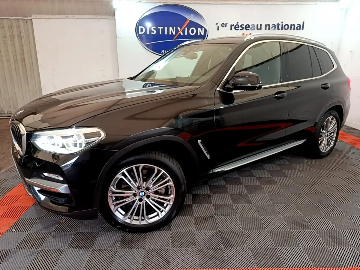 BMW X3 xDrive20d noir en 3/4 avant droit, avec jantes alliage et phares LED allumés dans showroom