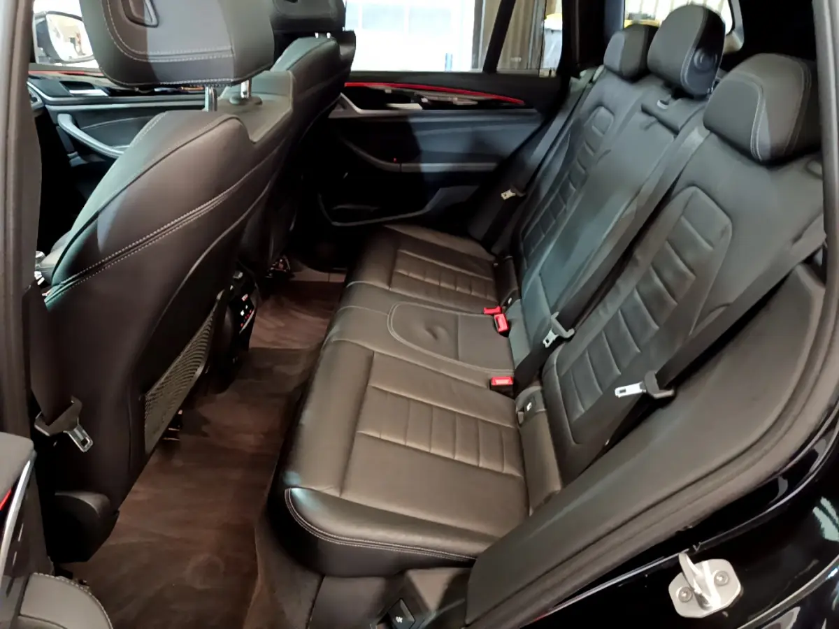 Vue côté droit de la banquette arrière en cuir noir du BMW X3 xDrive20d 2019 avec finitions Luxury et ceintures rouges.