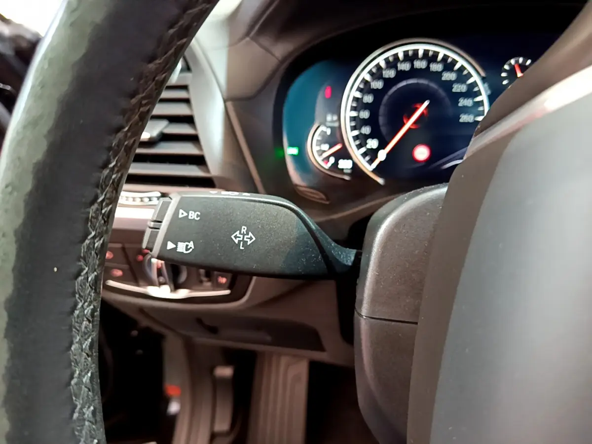 Vue rapprochée du commodo de clignotant à gauche sur le volant cuir d'un BMW X3 noir, tableau de bord éclairé.