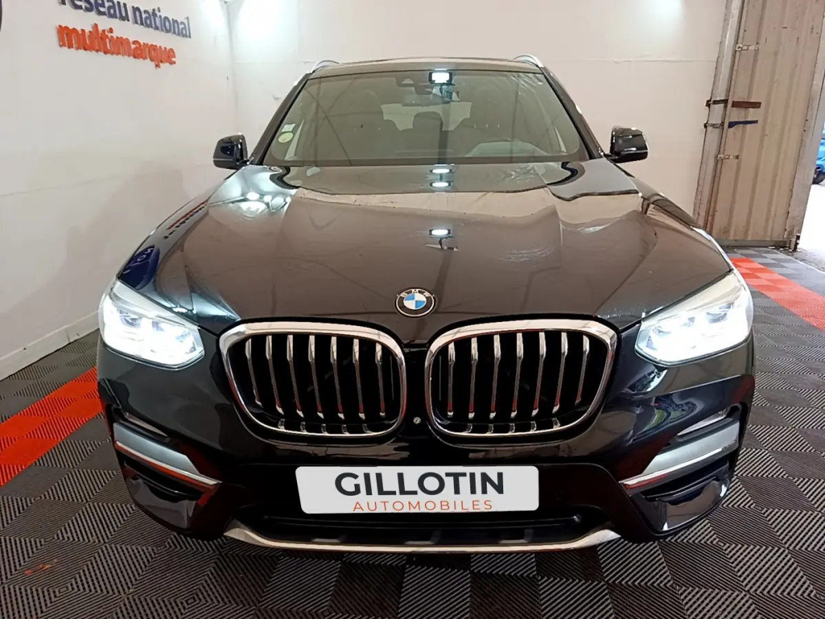 Vue frontale d'un BMW X3 noir avec phares LED allumés et calandre double haricot chromée dans un showroom.
