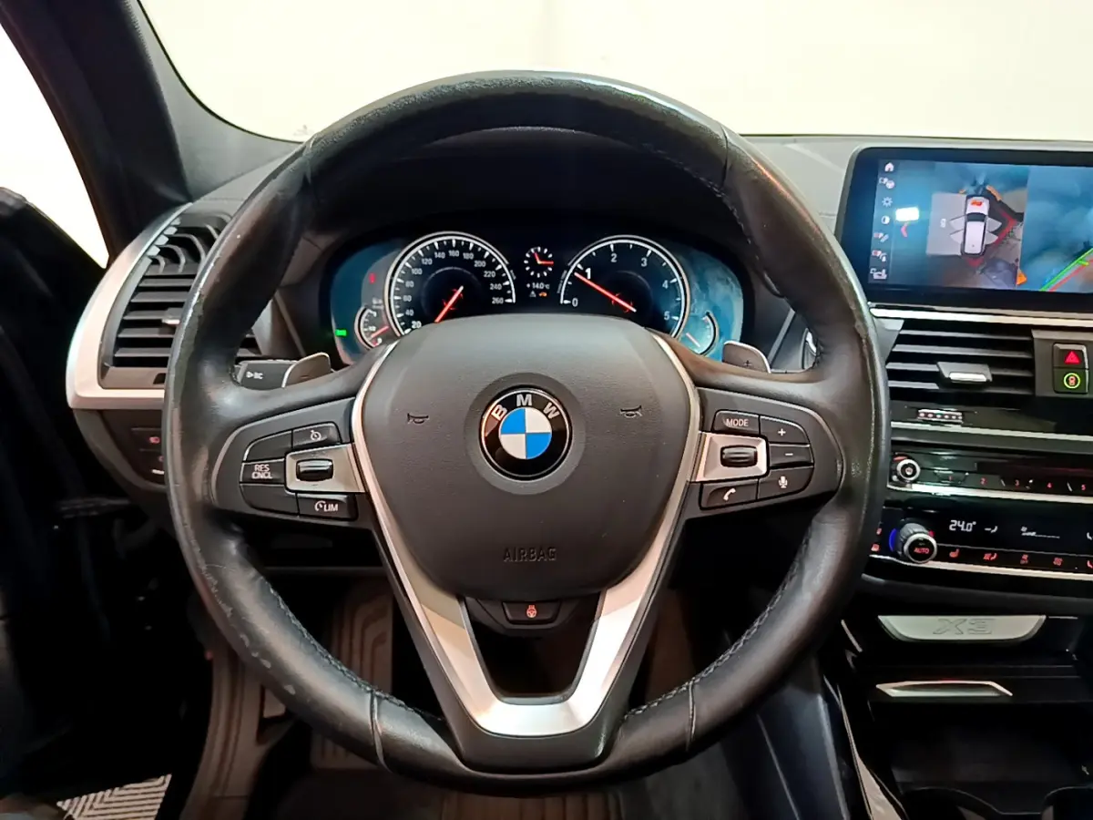 Vue rapprochée du volant cuir noir et du tableau de bord digital du BMW X3 xDrive20d 2019, avec écran tactile et affichage 3D.