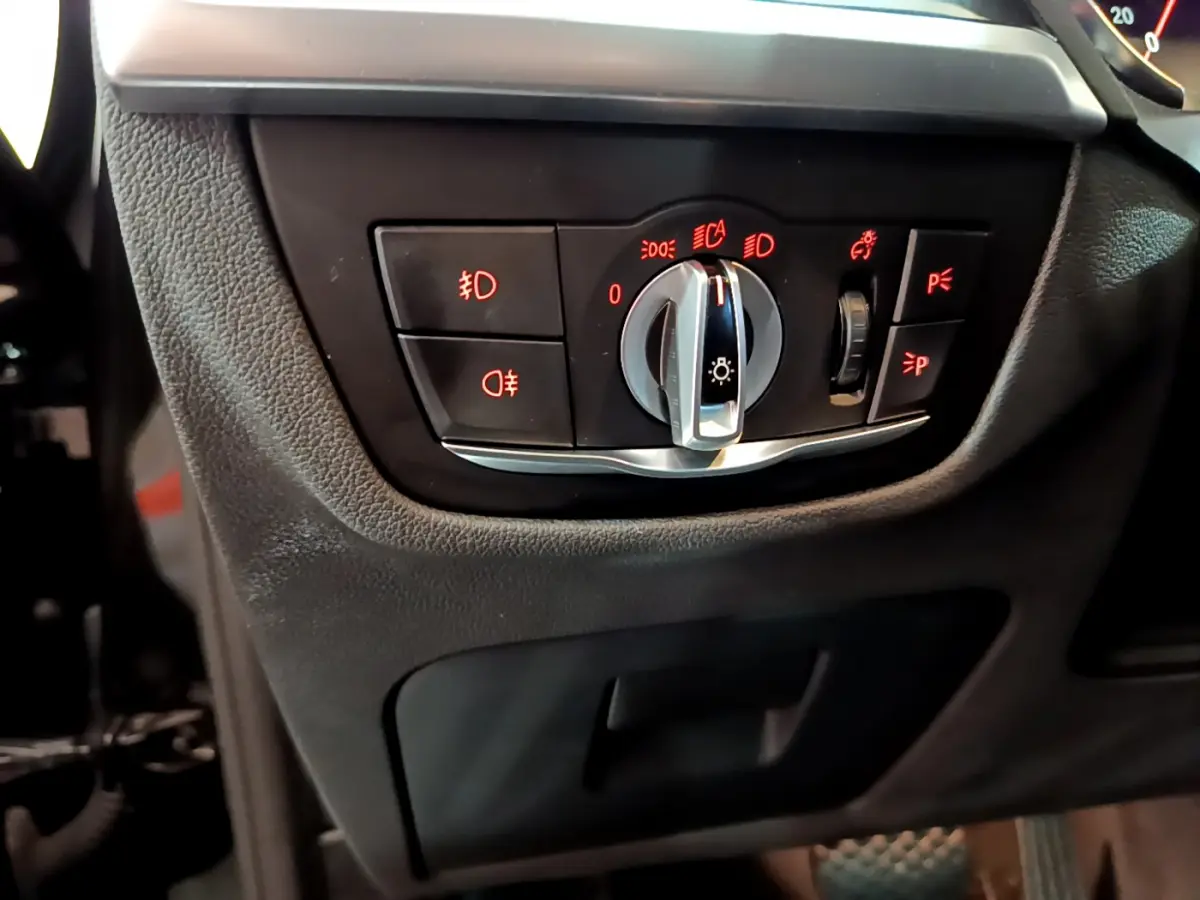 Gros plan sur la commande d'éclairage noire avec voyants rouges dans l'habitacle du BMW X3 noir 2019.