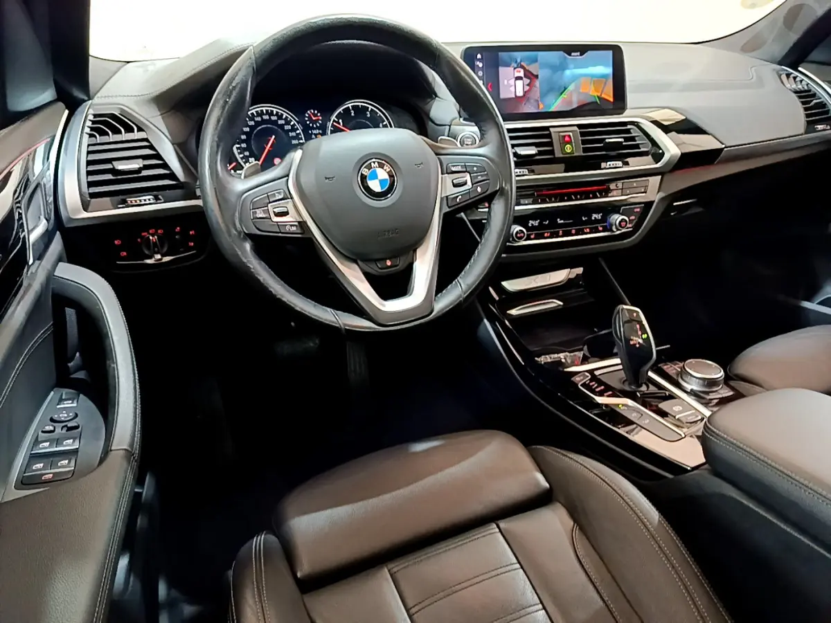 Vue intérieure côté conducteur du BMW X3 noir 2019, volant cuir, tableau de bord avec écran tactile et console centrale moderne.