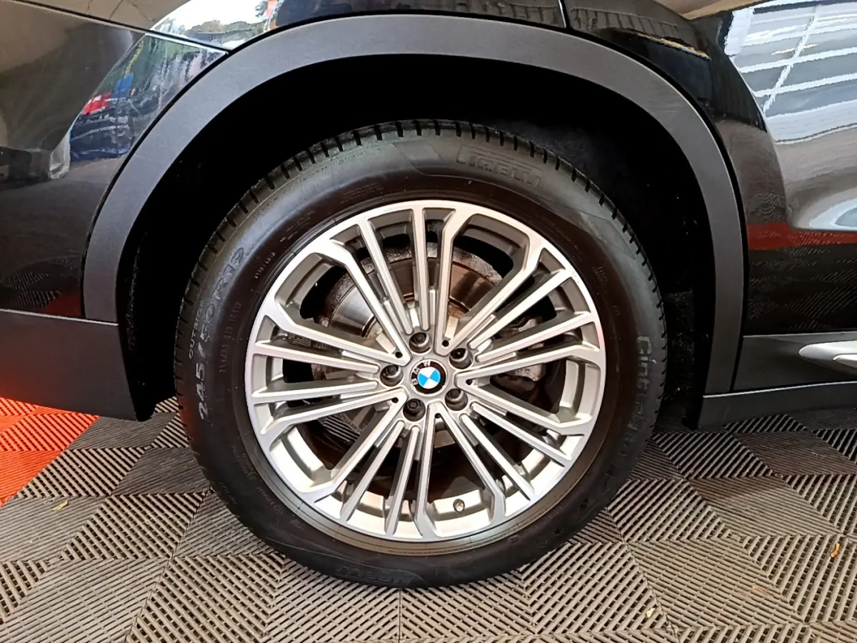 Gros plan sur la roue avant gauche du BMW X3 noir, mettant en valeur la jante alliage multi-branches et le logo central.