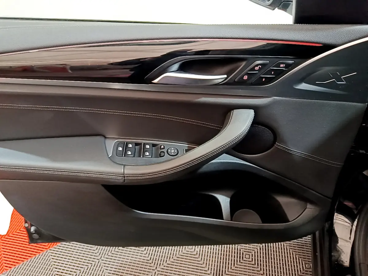 Gros plan sur la porte côté conducteur du BMW X3 noir 2019, avec commandes de vitres et logo X embossé.