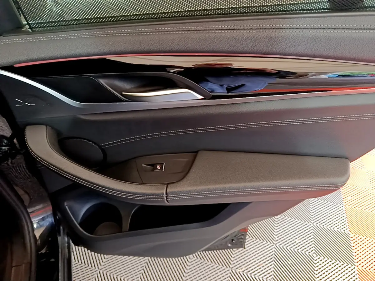 Gros plan sur la porte côté gauche intérieure noire du BMW X3 xDrive20d 2019 avec poignée argentée et coutures blanches.