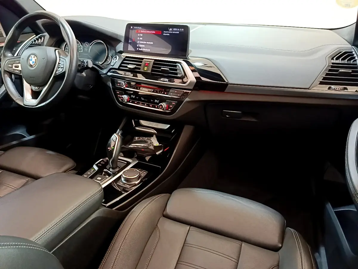 Intérieur BMW X3 xDrive20d 2019 vu côté conducteur, tableau de bord moderne avec écran tactile 10,3 pouces et cuir noir.