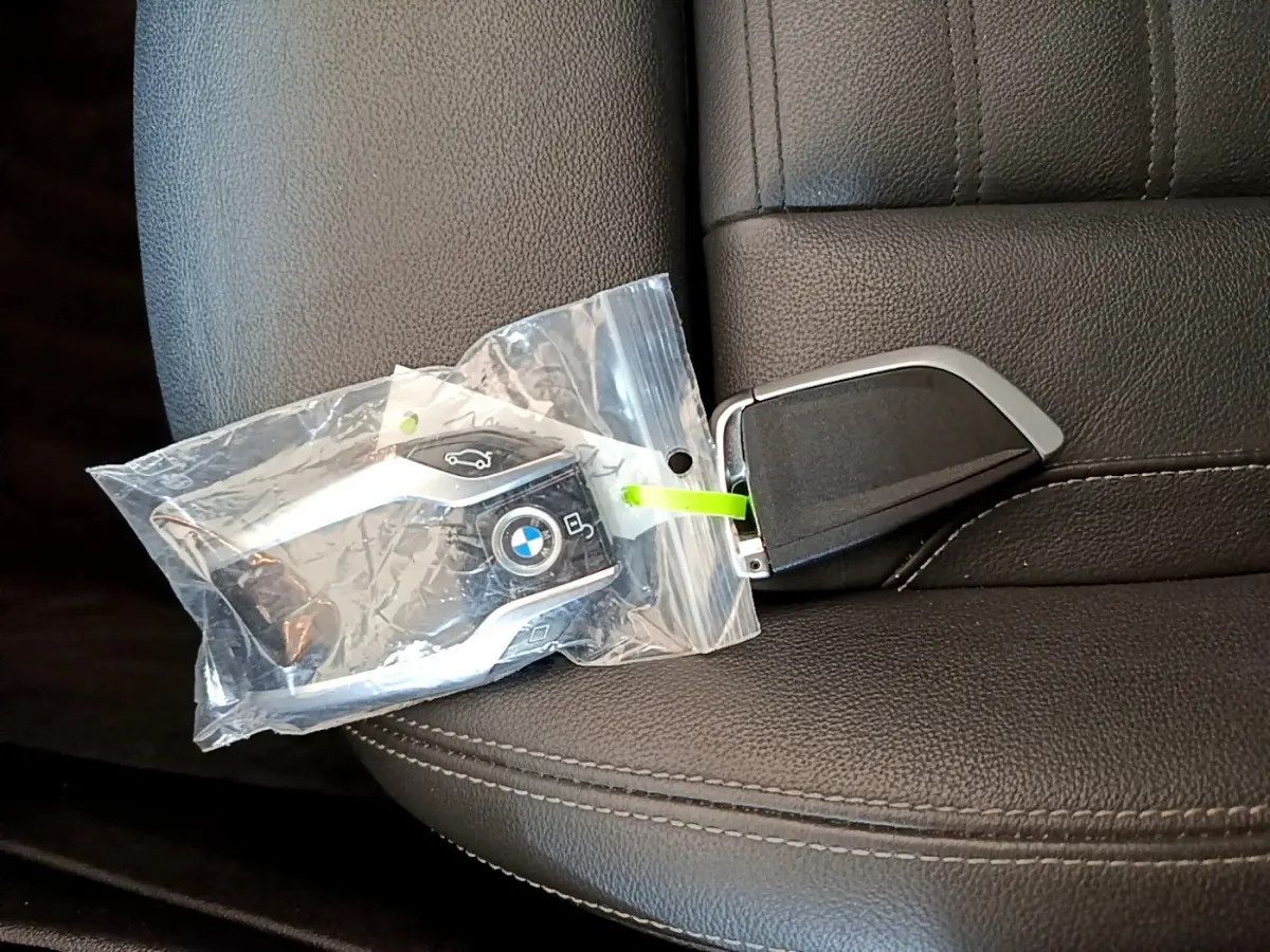 Clé BMW noire avec logo bleu et blanc posée sur un siège en cuir noir à coutures apparentes.