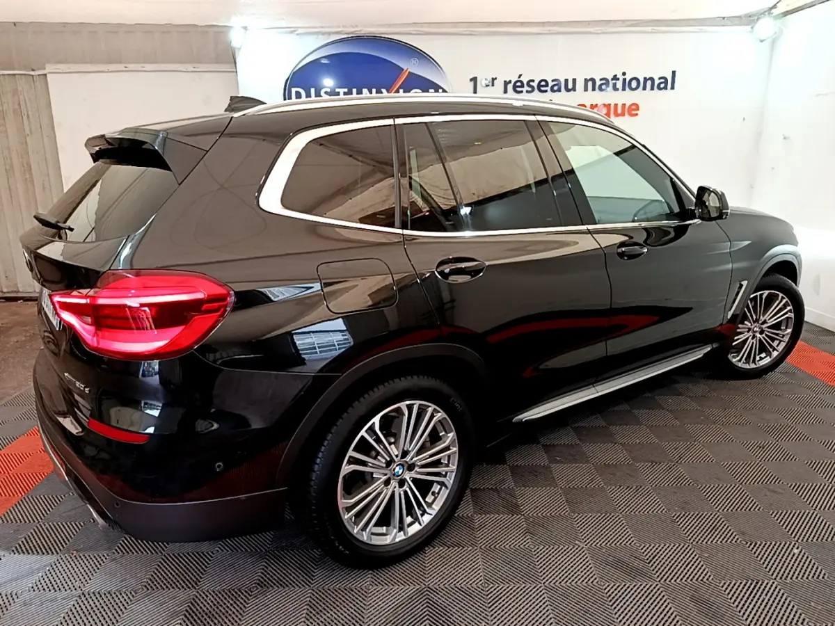 BMW X3 xDrive20d noir vu en 3/4 arrière droit, avec jantes alliage et feux arrière LED allumés.