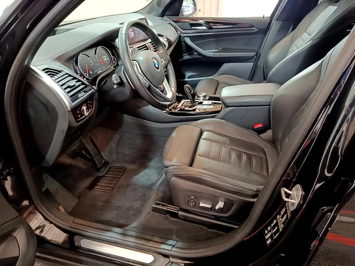 Intérieur noir vu côté conducteur d'une BMW X3 xDrive20d 2019, sièges cuir et tableau de bord moderne.