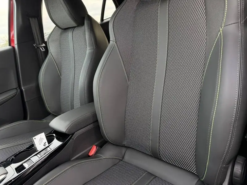 Gros plan sur les sièges avant noirs avec surpiqûres vertes du Peugeot 2008 1.2 Hybrid 145ch GT, intérieur moderne.