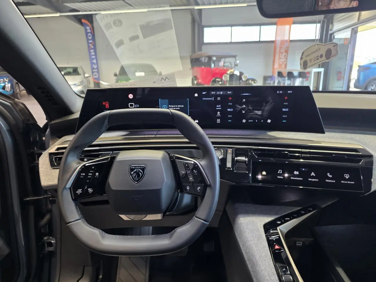 Vue intérieure du tableau de bord du Peugeot 3008 2025, volant compact cuir noir et écran panoramique incurvé.