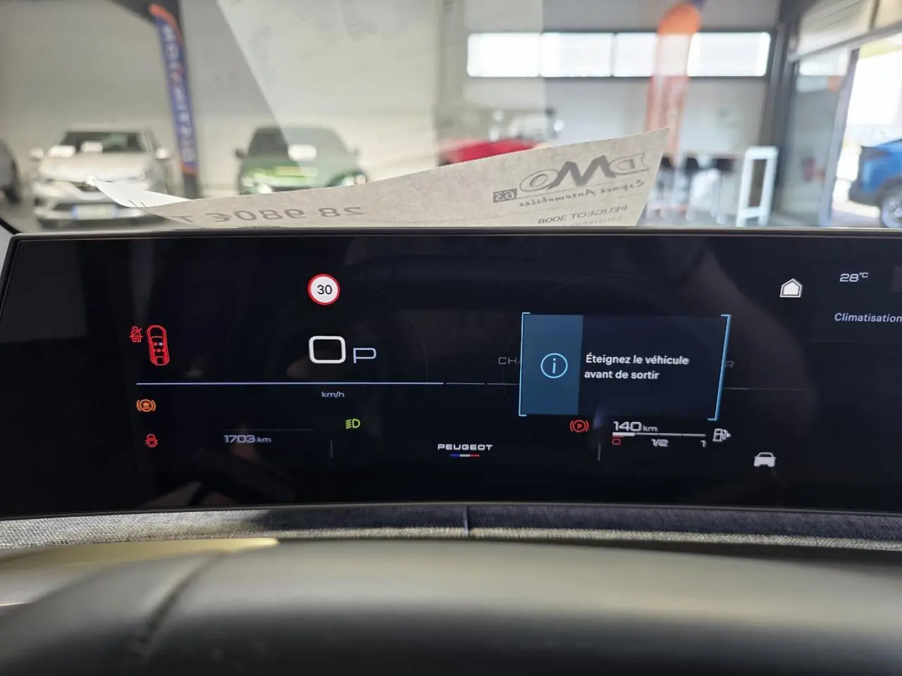 Vue rapprochée du tableau de bord numérique du Peugeot 3008 Hybrid 2025 avec affichage d'alerte et logo central.