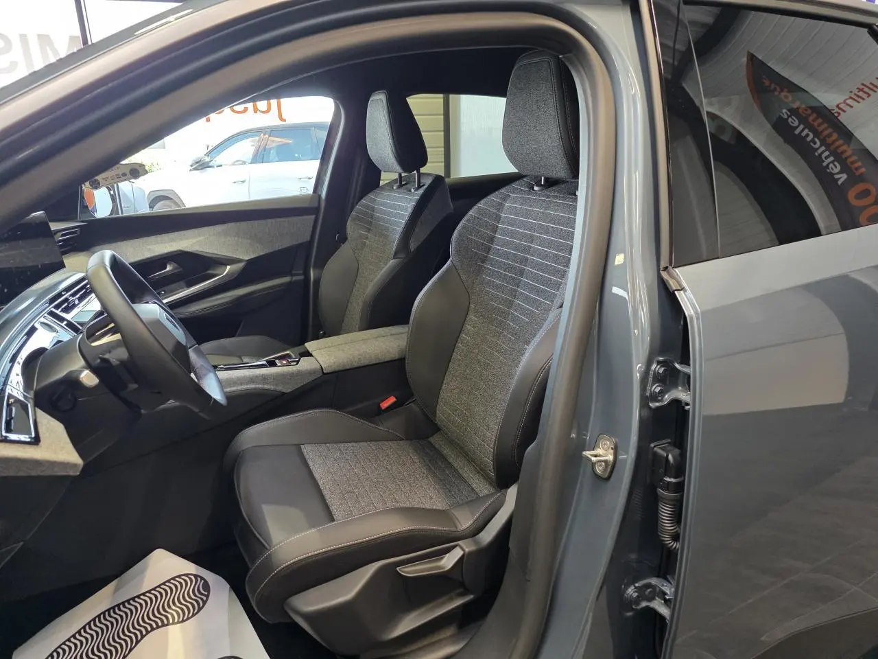 Vue intérieure côté conducteur du Peugeot 3008 hybride 2025 bleu clair, mettant en valeur les sièges tissu et cuir bicolores.