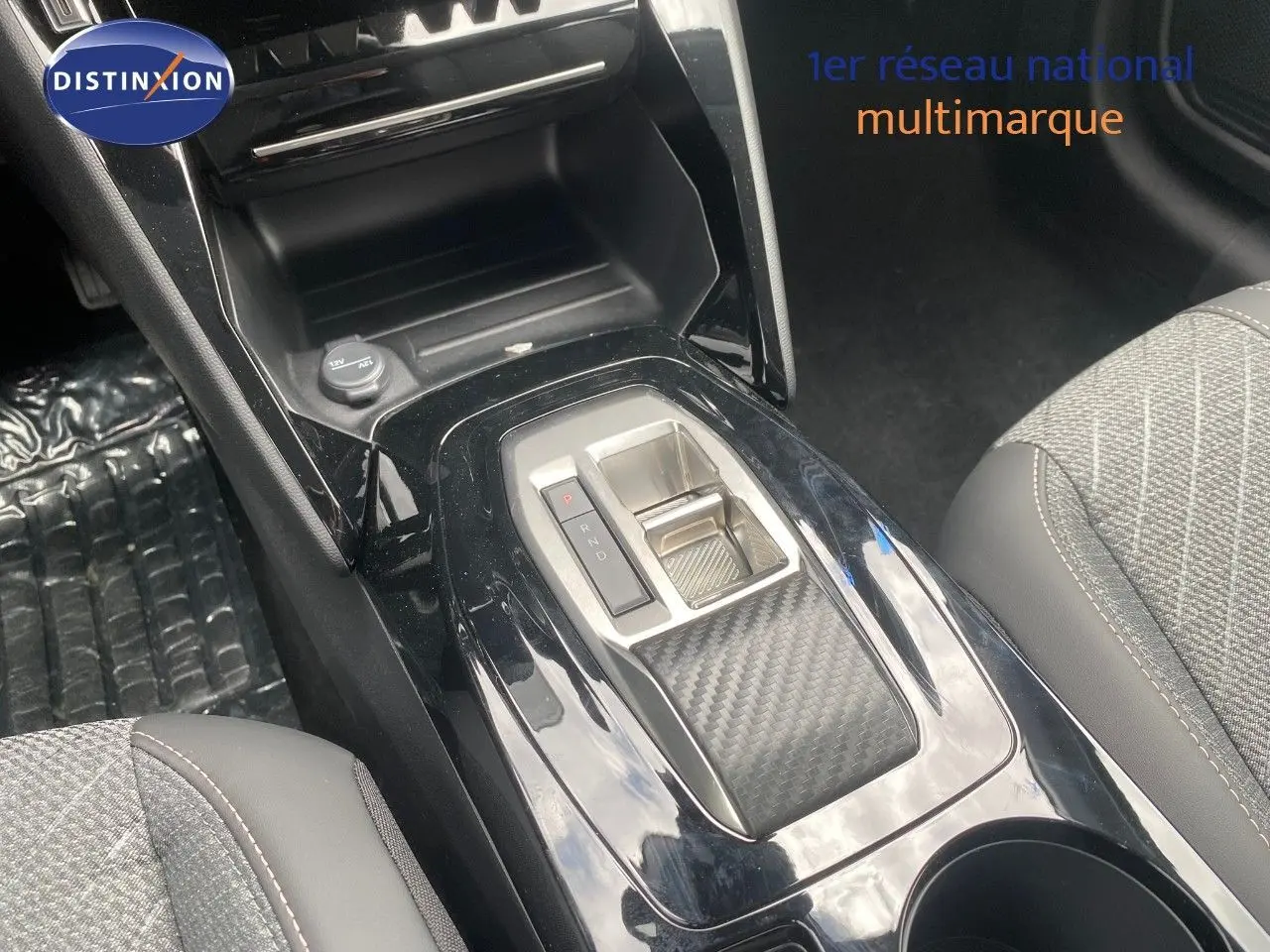Vue rapprochée de la console centrale noire brillante avec sélecteur de boîte auto et sièges tissu gris de la Peugeot 208 Hybrid 145ch.