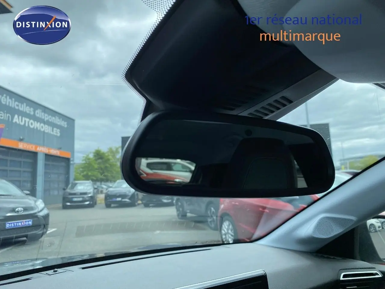 Vue intérieure du rétroviseur central d'une Peugeot 208 gris selenium, avec reflet du parking extérieur et autres véhicules visibles.
