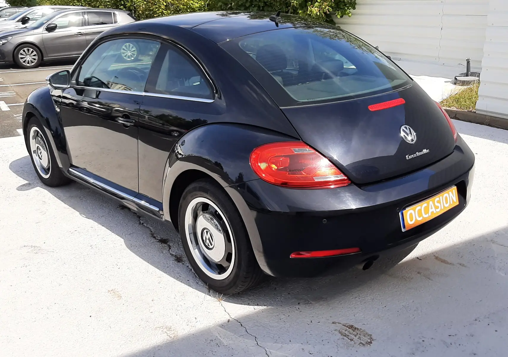 Vue 3/4 arrière droite d'une Volkswagen New Beetle noire de 2015, avec jantes d'origine et feux arrière rouges.
