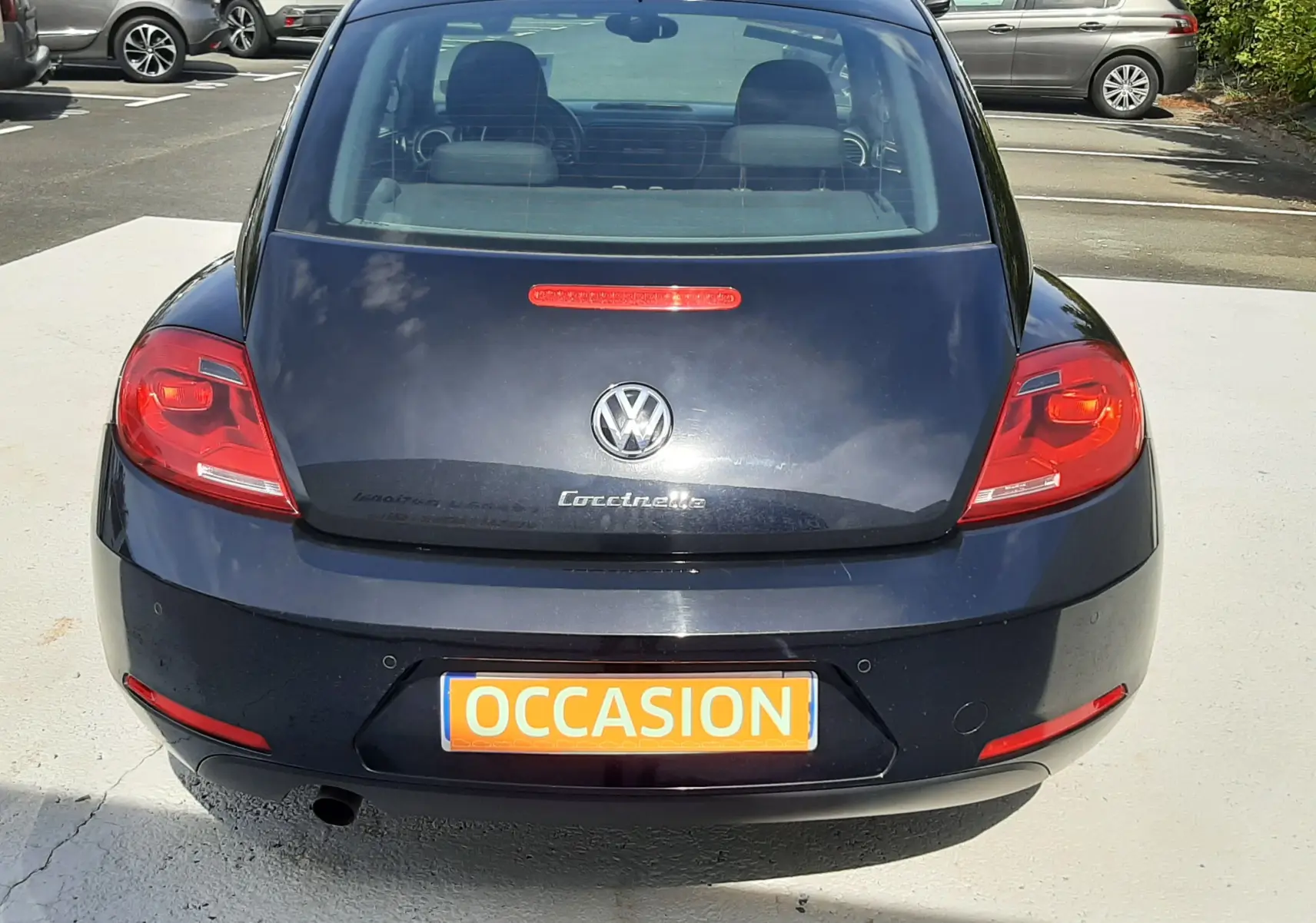 Vue arrière d'une Volkswagen New Beetle noire de 2015 avec plaque "OCCASION" en orange, stationnée en extérieur.