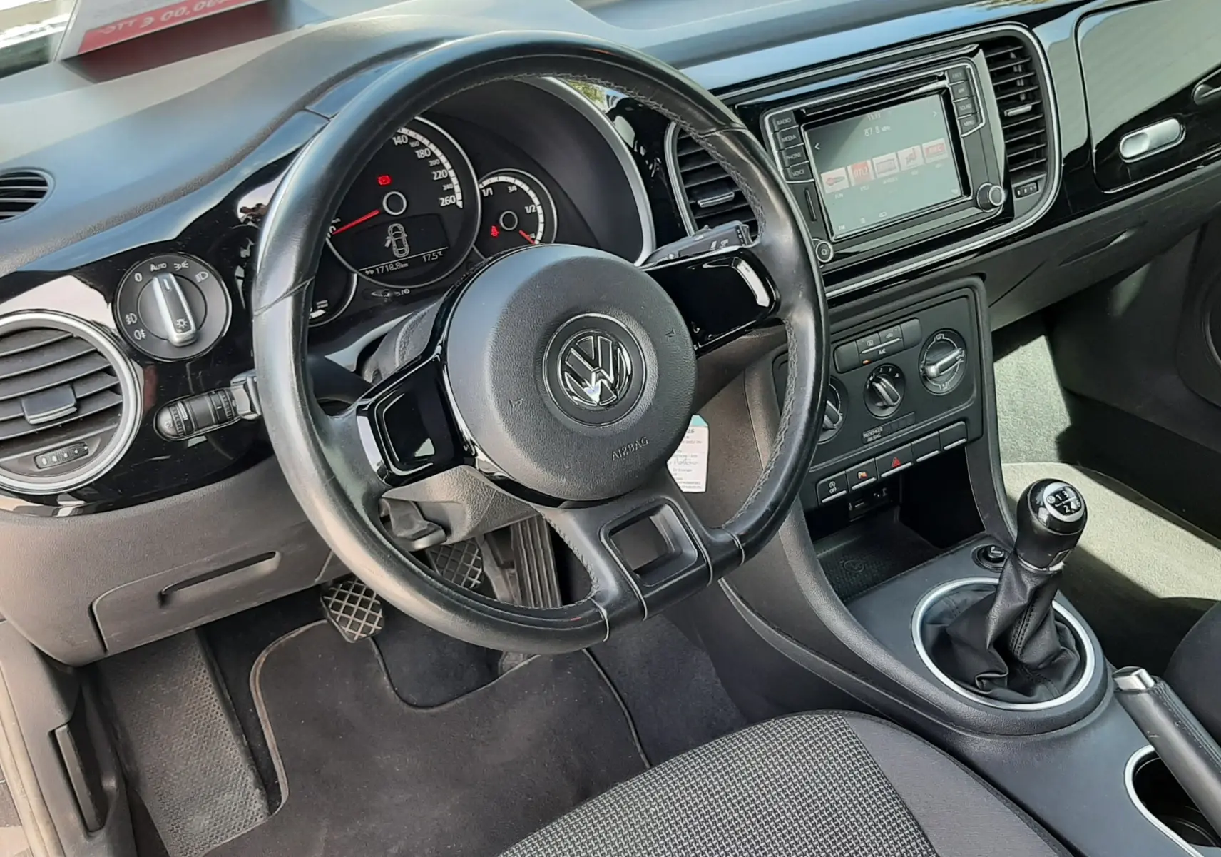 Vue intérieure côté conducteur du Volkswagen New Beetle noir, avec volant, tableau de bord et levier de vitesse manuel visibles.