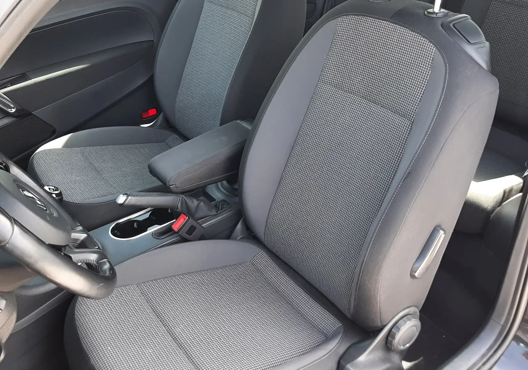 Vue intérieure côté conducteur du Volkswagen New Beetle noir 2015, sièges tissu gris avec accoudoir central.