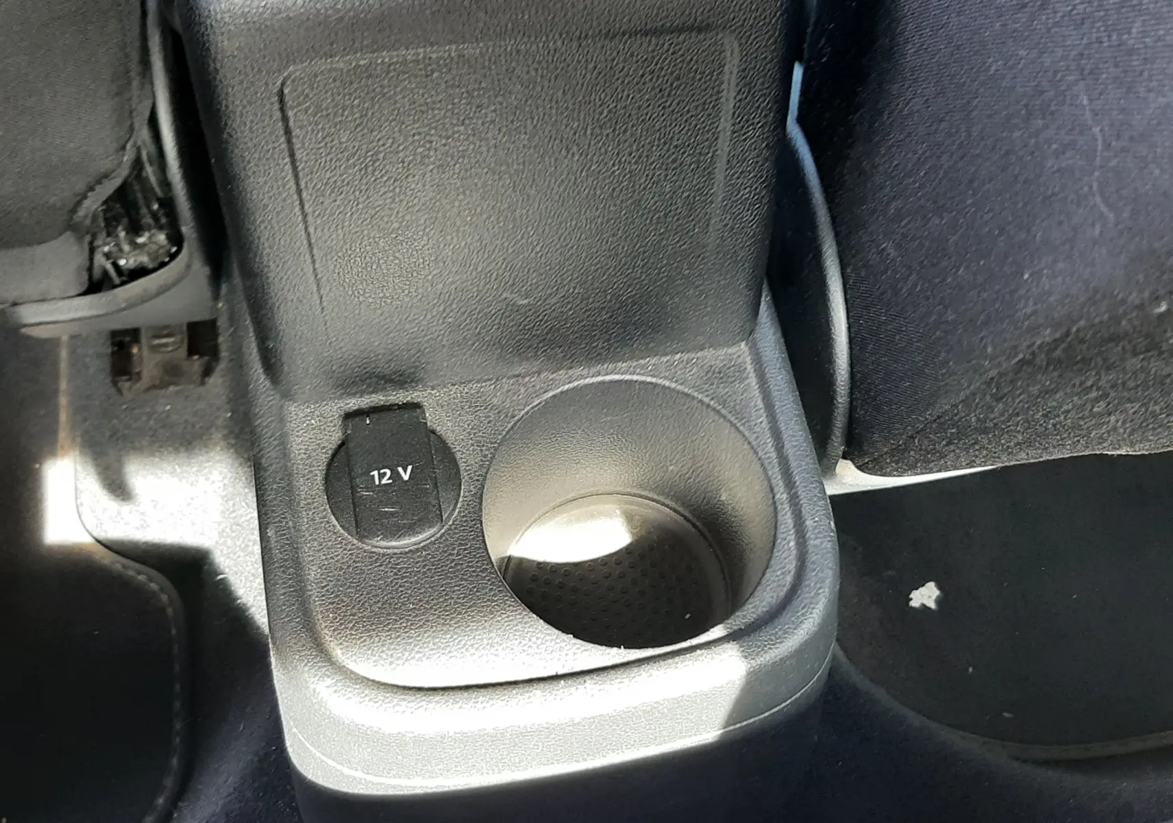Gros plan sur la console arrière noire du Volkswagen New Beetle 2015, avec prise 12V et porte-gobelet intégré.